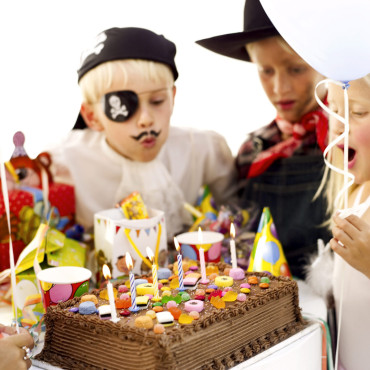 Children (6-10) Wearing Costumes and Blowing Out Candles on Birthday Cake --- Image by © Royalty-Free/Corbis
